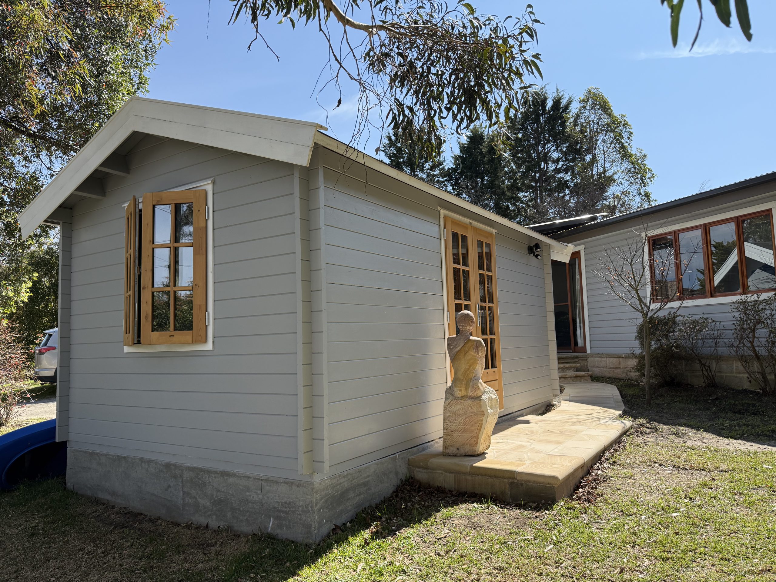 outside of woodland cabin used as backyard retreat with casement window and french doors and custom stone path
