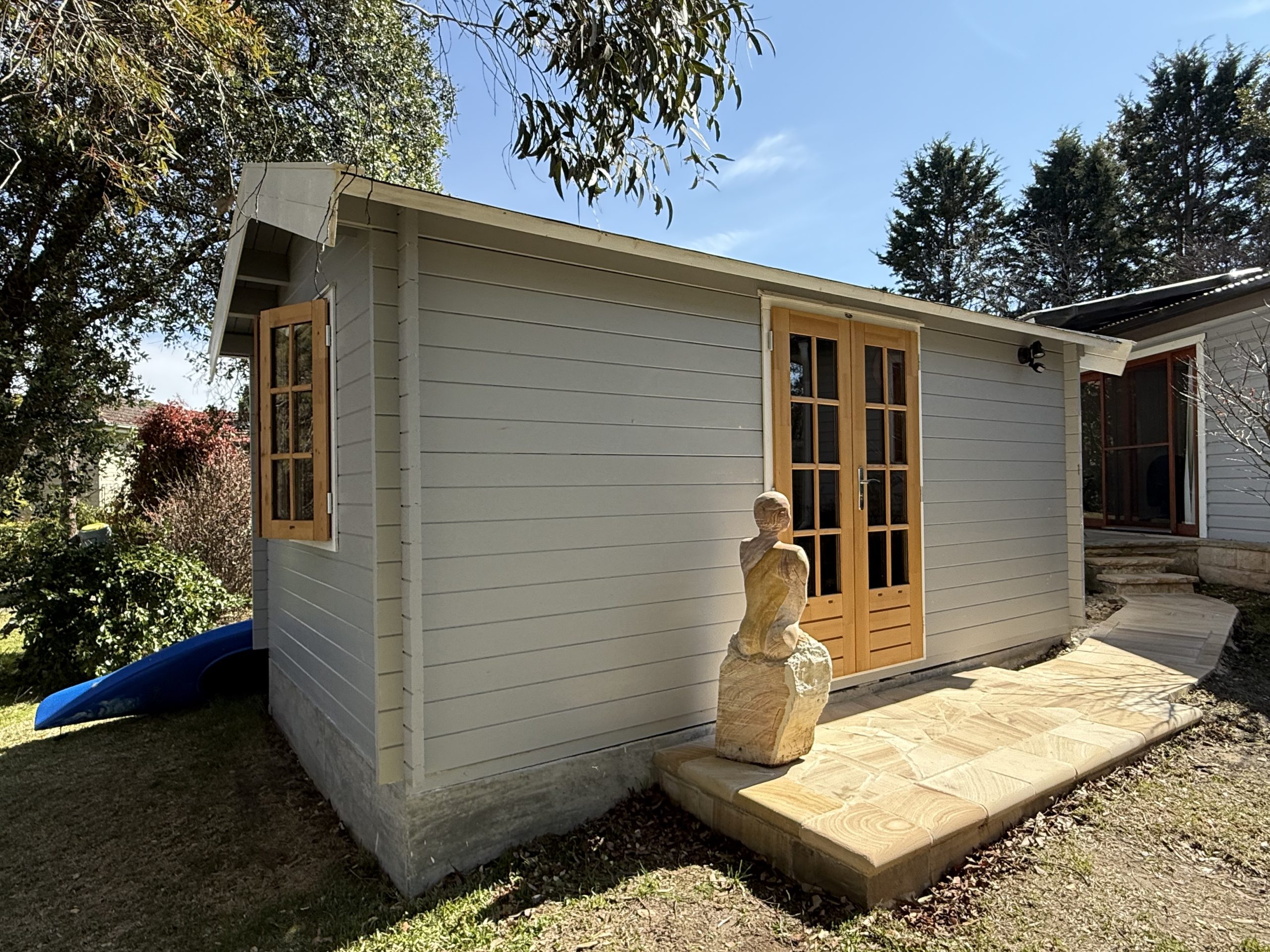 outside of woodland cabin used as backyard retreat with casement window and french doors and custom stone path