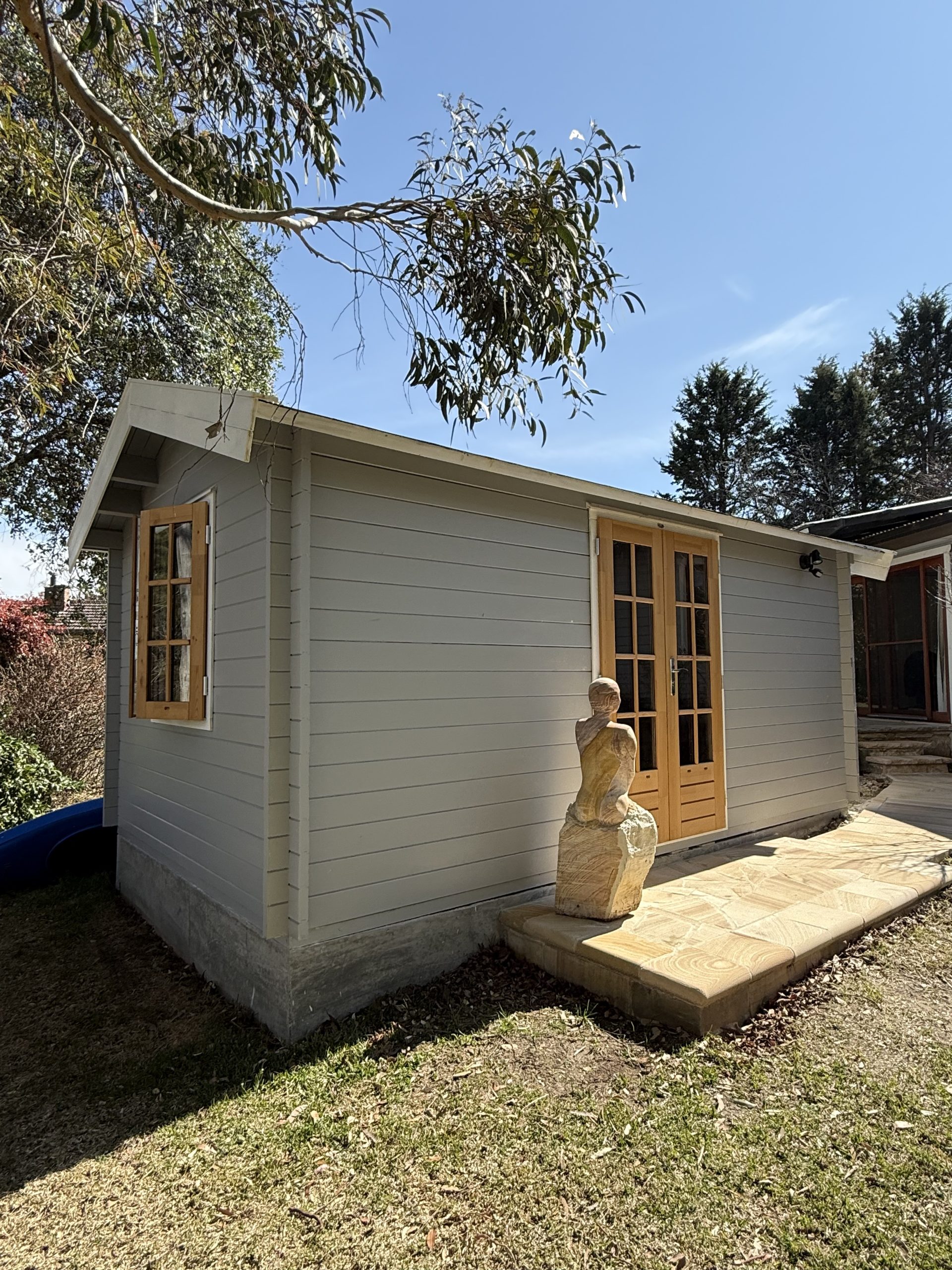 outside of woodland cabin used as backyard retreat with casement window and french doors and custom stone path